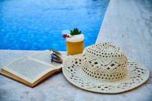 cocktail, livre et chapeau au bord d'une piscine